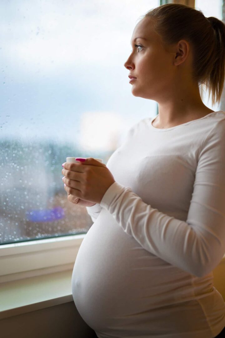Thoughtful pregnant woman looking out the window drinkng tea Thoughtful pregnant woman looking out the window drinkng tea